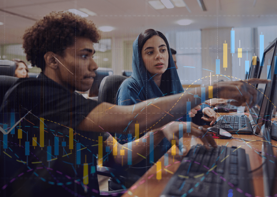 Two students work together at computers in a classroom, discussing data displayed on their screens. A transparent overlay of graphs and charts.