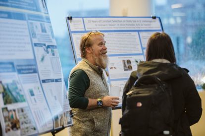 professor and student talking near a poster showing faculty research