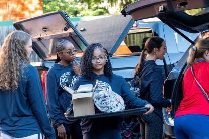 student holding a box and surrounded by cars at a college move in day on campus