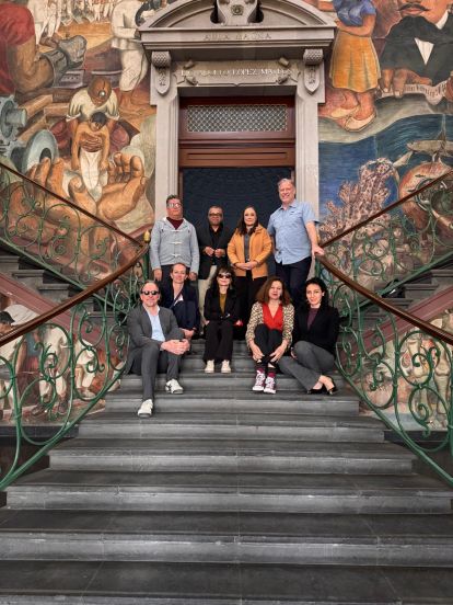 A group of people sitting and standing on the steps in front of a colorful mural.